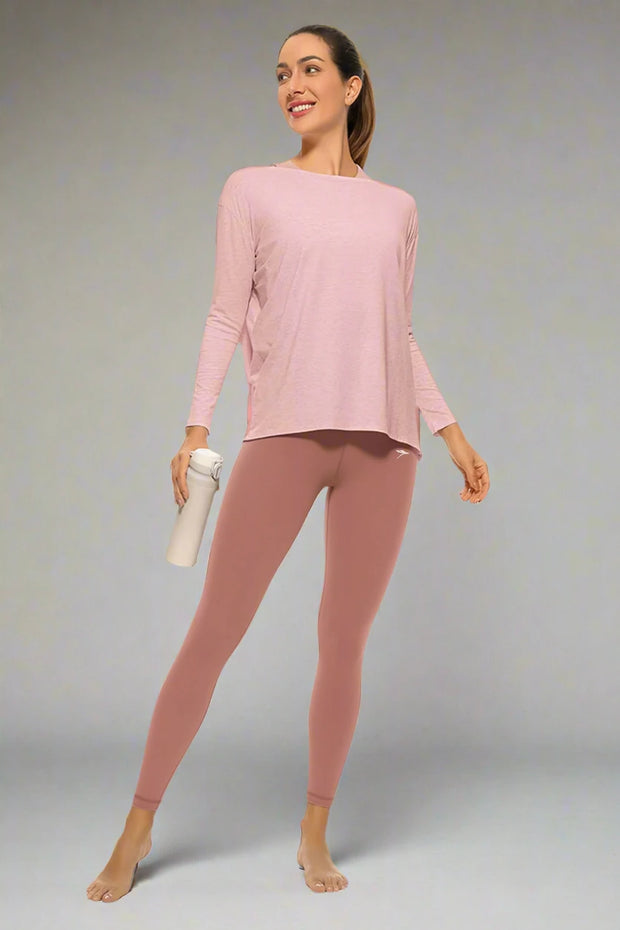 Woman wearing a pink long-sleeve top and leggings holding a white water bottle on a white background